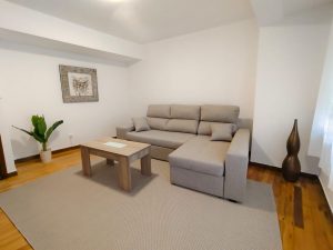 Salón luminoso con sofá chaise longue gris, mesa de centro de madera y planta decorativa en piso de alquiler en Carballo - Serdava