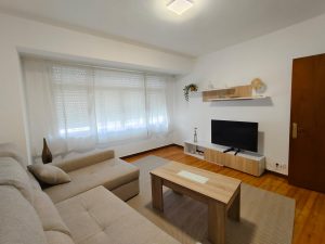 Salón luminoso con sofá en L, mesa de centro de madera y mueble de televisión en piso de alquiler en Carballo - Serdava