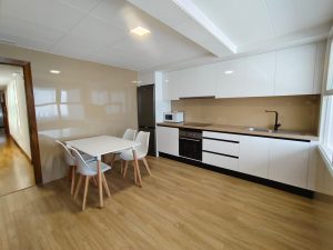 Cocina moderna con muebles blancos, mesa de comedor y suelo de madera en piso de alquiler en Carballo - Serdava