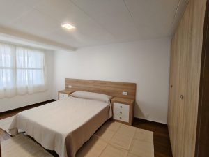 Dormitorio luminoso con cama de matrimonio, cabecero de madera, mesitas de noche y armario empotrado en piso de Carballo - Serdava
