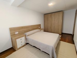 Dormitorio con cama de matrimonio, cabecero de madera, mesita blanca y armario empotrado en piso de alquiler en Carballo - Serdava