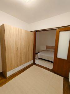 Habitación con armario de madera y puerta corredera que conecta con un dormitorio con cama en piso de alquiler en Carballo - Serdava