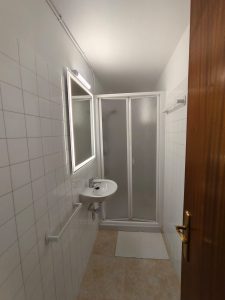 Baño moderno con ducha, lavabo con espejo iluminado y azulejos blancos en piso de alquiler en Carballo - Serdava