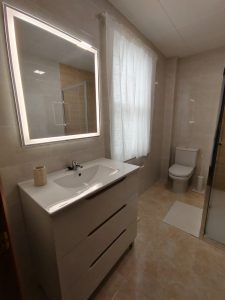 Baño moderno con mueble de lavabo, espejo con luz LED y sanitario en piso de alquiler en Carballo - Serdava