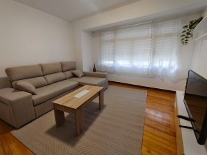 Salón luminoso de piso en alquiler en Carballo con sofá chaise longue, mesa de centro de madera y suelo de parqué - Serdava