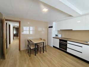 Cocina moderna con muebles blancos, mesa de comedor y acceso a pasillo en piso de alquiler en Carballo - Serdava