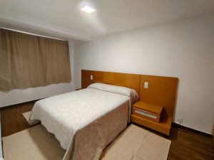 Dormitorio con cama de matrimonio, cabecero de madera y suelo de parquet en piso de alquiler en Carballo - Serdava
