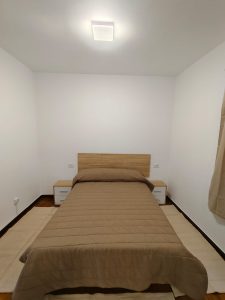 Dormitorio luminoso con cama individual, cabecero de madera y mesitas de noche en piso de alquiler en Carballo - Serdava