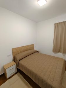 Dormitorio con cama de matrimonio, cabecero de madera y mesita de noche en piso de alquiler en Carballo - Serdava