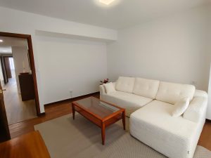 Salón luminoso con sofá esquinero blanco y mesa de centro de madera en piso de alquiler en Carballo - Serdava