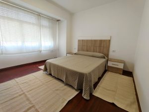 Dormitorio luminoso con cama de matrimonio, cabecero de madera y mesitas de noche en piso de alquiler en Carballo - Serdava