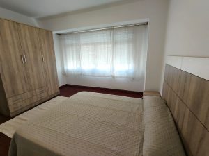 Dormitorio luminoso con cama de matrimonio, armario de madera y gran ventanal en piso de alquiler en Carballo - Serdava
