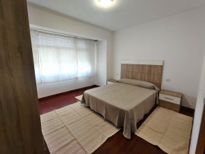 Dormitorio principal con cama de matrimonio, cabecero de madera y ventanal luminoso en piso de alquiler en Carballo - Serdava